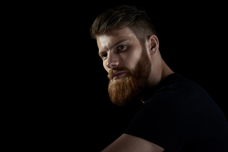 Dramatic light studio shot of young caucasian bearded stylish man Handsome hairstyling male portrait over black background Free copy space template.の写真素材