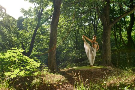 Young attractive asian woman practicing yoga, doing exercise working out in the forest, wearing sportswear, pants and top. Young sporty woman practicing yoga on beautiful sunset forestの写真素材