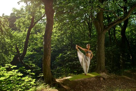 Asian woman doing balance on one leg Asana yoga pose Beautiful portrait of yoga Outdoors lifestyle portrait. Summer relaxation Nature background Healthy lifestyle Outdoor activity Yoga in modern styleの写真素材