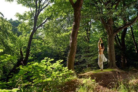 A woman practices yoga alone in the forest turning back Harmony with nature Female symbol. Yoga in modern style. Asana yoga pose Spiritual and emotional concept. Sensitivity to natureの写真素材