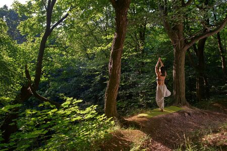 Woman practices yoga alone in the forest Back view Outdoor activity Young attractive asian woman practicing yoga, doing exercise working out Woman is meditating alone at sunriseの写真素材