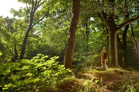 Woman sitting in yoga pose with namaste facing the sun Modern for lifestyle design. Healthy fitness background. Body relaxation. Asana yoga pose. Outdoors lifestyle portrait Vacation summer relaxationの写真素材