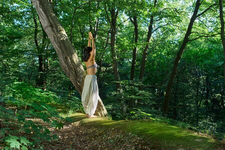 A woman practices yoga alone in the park. Side view. Harmony with nature Surya Namaskar Asana yoga pose. Outdoors lifestyle portrait. Vacation, summer, relaxation. Nature background. Healthy lifestyleの写真素材