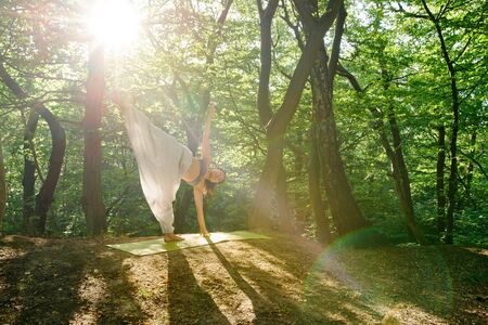 Young yogi asian attractive woman practicing yoga concept, standing in Half Moon exercise, Ardha Chandrasana pose, working out, . A woman practices yoga alone in the forest.の写真素材