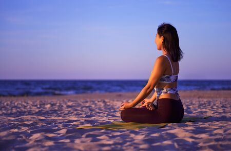 Woman meditates while practicing yoga by the sea at sunset. Freedom concept. Calmness and relax, woman happiness. Body relaxation. Asana yoga pose. Beautiful portrait of yoga. Outdoors lifestyle.の写真素材