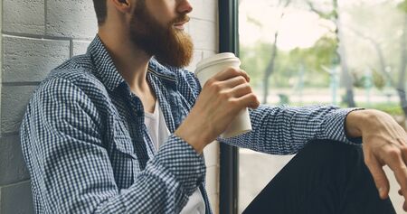Close up of a beard of a young man. Young attractive bearded man rests and looks out the window. Enjoy the morning. Drink fresh bracing coffee looking into the distance. Wide shotの写真素材