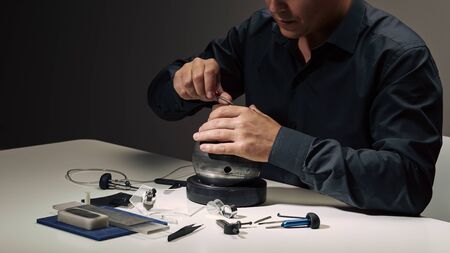 Professional engraver tools for jewelleries manufacturing on white desk. Craftsman, engraver, goldsmith workplace. Mans hand closeup. Low light dramatic photo Jewelry craftsmanship, engraving concept.の写真素材