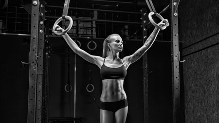 Fitness girl exercising with gymnastic rings in gym. Female crossfit athlete in black sportswear...