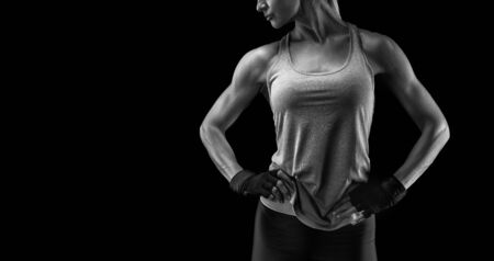 Fitness woman in sports tank top, short sleeve tee, gloves. Black and white close-up photo with copy space on left. Her hands on hips.の写真素材
