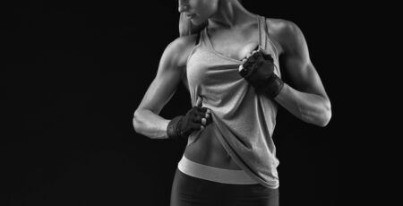 Close-up black and white photo of muscular woman with gloved hands showing off her strong and fit body. Active lifestyle concept. Fit body workout abs training. Girl sport weight loss success.の写真素材