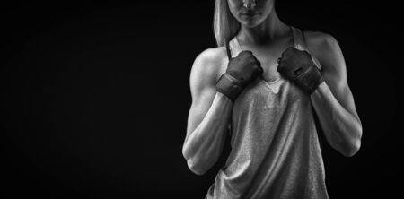Black and white portrait of young woman with muscular body standing against black background. Image of fitness woman in sports clothing and gloves.の写真素材