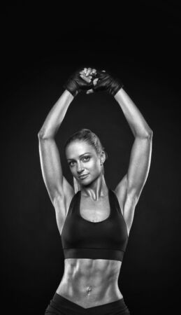 Black and white vertical image of fit female model with perfect torso in studio. Sensual young female in black sportswear posing in black background with copy space.の写真素材