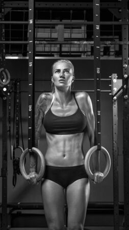 Working out Young athletic sportswoman exercising on gymnastic rings at gym Exercising woman holding gymnast rings and looking up. Workout at gym. Black and white vertical photo.の写真素材