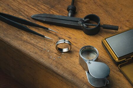 Workplace of a jeweler. Tools and equipment for jewelry work on an antique wooden desktop. Jeweller, engraver at work on jewelry made of diamonds and gold. Wood Platinum Diamond Metal Backgroundの写真素材