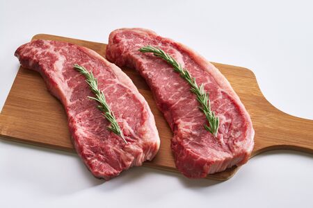 Raw beef steak ready to be cooked. Photo of two fresh raw striploin steak on wooden board on white background with rosmary.の写真素材