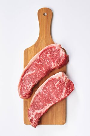 Photo of two fresh raw striploin steak on wooden board on white background. Raw juicy beef steak ready to be cooked. Top view food preparation process concept.の写真素材