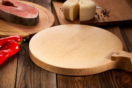 Empty serving board is on a wooden table with ingredients around. Tasty filling: fresh fish, feta cheese, red bell pepper. and round cutting board Background with cutting board on wooden tableの写真素材