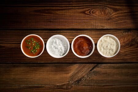 Top view of a set of 4 sauces. Bowls with sauces on wooden table An even row of cups with white and red sauces Set of different delicious sauces on vintage wooden table, top viewの写真素材