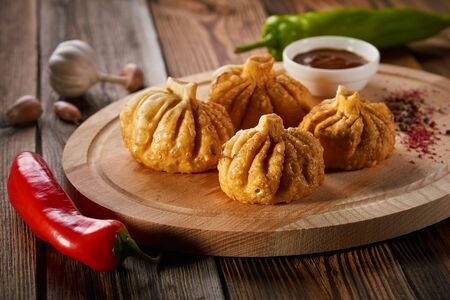 Georgian deep-fried Khinkali dumplings with meat and red pepper, on a wooden cutting board. Traditional dish of Caucasian cuisine. Concept of diet and healthy eating.の写真素材