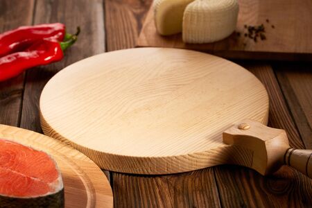 Empty serving board is on a wooden table with ingredients around. Tasty filling: fresh fish, feta cheese, red bell pepper. Wooden background with wooden table, tablecloth and round cutting boardの写真素材