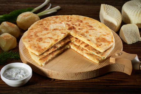 Sliced pies with various fillings and feta cheese. Traditional Caucasian cuisine. Stack of baked pies on a plate Sauce and ingredients on a vintage table The concept of diet and healthy eatingの写真素材