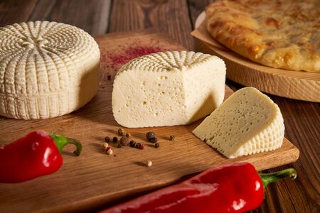Sliced round white homemade cheese - traditional milk creamy dairy product on vintage wooden board. Rustic style. Feta cheese served with red peppers on vintage wooden board National Georgian cuisineの写真素材