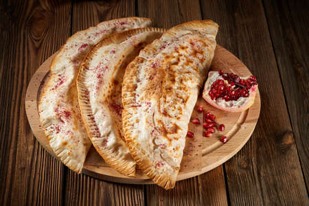 Caucasian food. Uzbek eastern Tatar cuisine, deep fried chebureki with meat on a wooden table, pomegranate. Deep fried turnovers or chebureki Fried pies with meat - chebureks oriental cuisineの写真素材