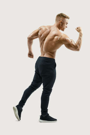 Strong back of a athletic muscular man flexing his arms against grey background. Rear view of handsome young shirtless fitness model with masculine physique in silhouette. Image with clipping path on white background.の写真素材