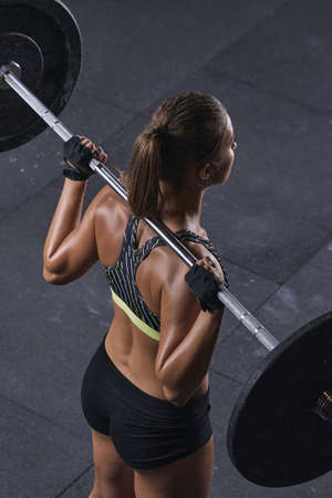Fitness woman lifting a weight in gym. Beautiful young girl getting ready to do barbell squats wearing a top. Close-up cover concept.の写真素材