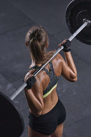 Close-up photo of attractive fitness model workout with barbell Sporty woman with perfect shoulders, biceps and triceps muscles Vertical photo.の写真素材