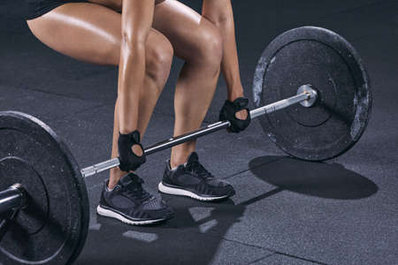 Close up of woman bodybuilder prepare to do exercises with barbell in a gym.の写真素材