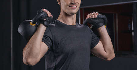 Sportsman workout with kettlebell. Smiling young male bodybuilder in gray t-shirt lifts weights in the gymの写真素材