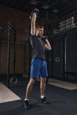 Portrait of athlete holding a kettlebell exercising crossfit at the gym. Handsome man doing functional training. Practicing workoutの写真素材