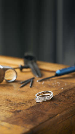 Vertical photo of a jeweler engraver tools and golden ring, diamonds on wooden vintage desk.の写真素材
