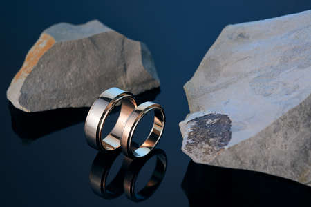 Two wedding rings among stones on the black polishedの写真素材