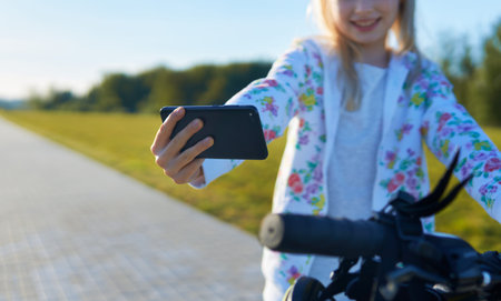 Portrait of a cheerful young caucasian girl on a bicycle holding a smartphone in his hand
