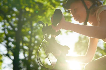Happy teenager girl rides best bike on a summer sunny day in a city park. Against the background of green leaves of trees. Urban biking - teen and bike in city park. Focus on handの写真素材
