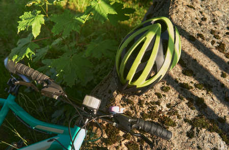 A light green bicycle helmet lies on a large stone in the park. Next to the grass lies a blue teenage bike. The concept of an active lifestyle and a safe ride.の写真素材
