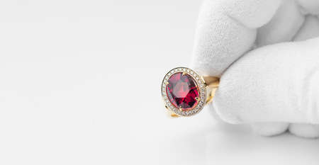 Golden ring with rhodolite gem and diamonds in jeweler hand in a white glove. Copy free space on left. concept for jeweler or shopの写真素材