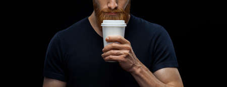 Croped shot of young caucasian bearded stylish man with paper cup of coffee to go over black background. Coffee to go concept.の写真素材