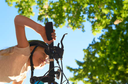 Little caucasian girl with blond hair rushes on a bicycle on a sunny summer day. View from the bottom. Focus on the hand. Urban biking - teen and bike in city park.の写真素材