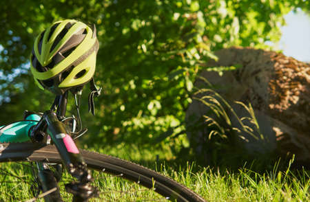 Close up photo of blue teenage bike lies on green grass. Bicycle helmet hanging on the handlebar. Bicycle lies on the ground in a city park Safe ride concept. Focus on the bicycle helmet.の写真素材