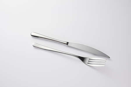 Stylish classy elegant metallic eating knife and fork cutlery for dining kitchen utensils Isolated on a white background, well lit. Kitchen set Flatware on white.の写真素材