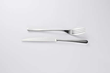 Stylish classy elegant metallic eating knife and fork cutlery for dining kitchen utensils Isolated on a white background, well lit. Kitchen set Flatware on white.の写真素材