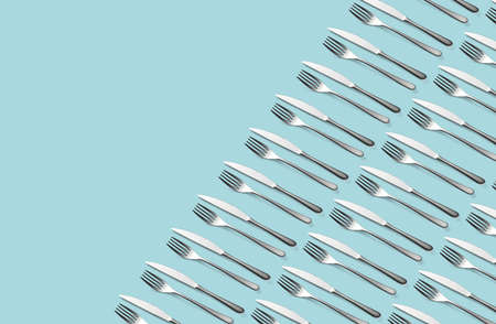 Knife and fork flat lay pattern on pastel blue background. Many metallic forks, and knives top view concept. Background for menu. Restaurant backdrop. Creative top view pattern. Copy free space.の写真素材