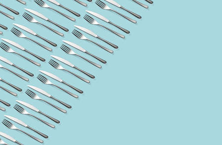 Knife and fork flat lay pattern on pastel blue background. Many metallic forks, and knives top view concept. Background for menu. Restaurant backdrop. Creative top view pattern. Copy free space.の写真素材
