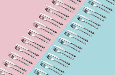 Knife and fork flat lay pattern on pastel pink and blue background. Many metallic forks, and knives top view concept Background for menu Restaurant backdrop. Creative top view pattern Copy free space.の写真素材