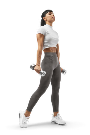 Bodybuilder with an athletic body lifted her head up holding dumbbells in hands. Sports, healthy lifestyle, beautiful thin figure and muscular body. Athlete in sports uniform workout with dumbbells.の写真素材