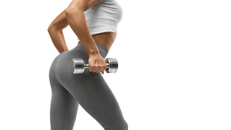 Fit, young and sexy female body. Sporty woman workout with dumbbells. Fitness model in leggings with beautiful buttocks. Sporty booty isolated on white background. Strength and motivation.の写真素材