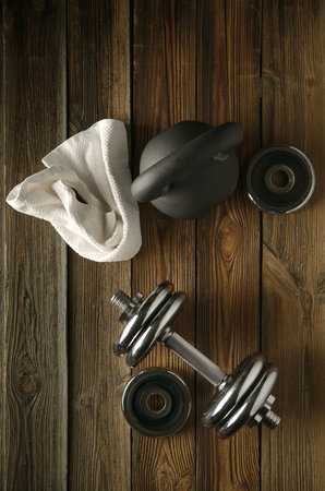 Black iron kettlebell, dumbbell and white towel on wooden floor in gym. Fitness equipments background Top view.の写真素材